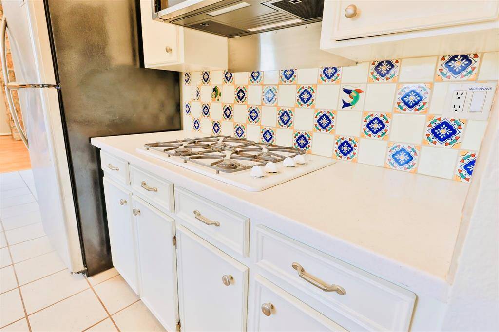 This kitchen features a gas cooktop with a colorful, patterned tile backsplash that adds a vibrant touch. It has white cabinetry and a stainless steel refrigerator, creating a bright and inviting space.
