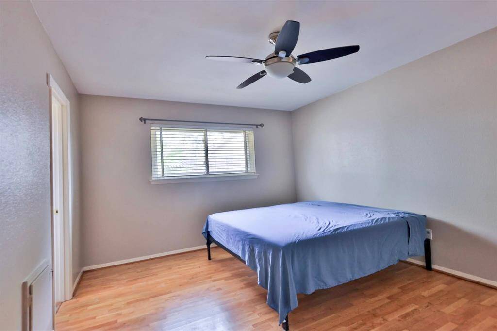 Bright bedroom with hardwood floors, neutral walls, ceiling fan, and a large window. Simple and clean layout.