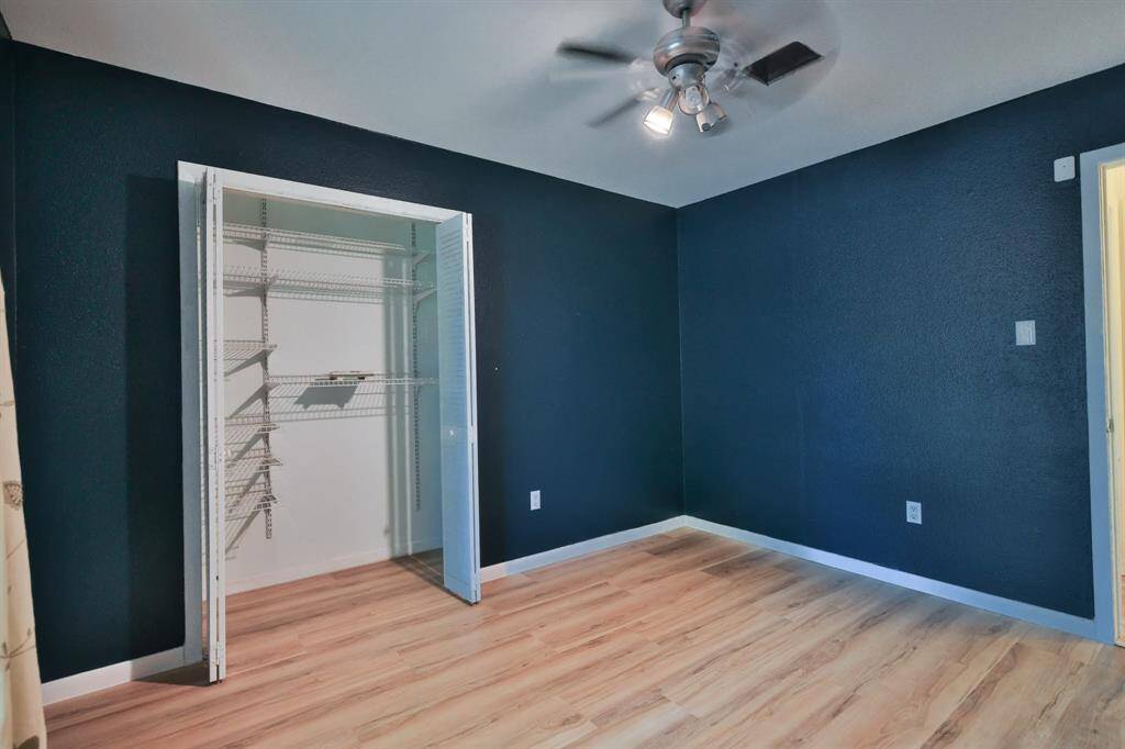 This room features dark blue walls, light wood flooring, a ceiling fan with lights, and a white closet with built-in shelving, offering a modern and functional space.