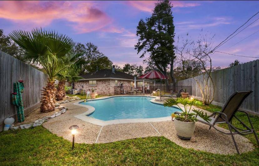 This inviting backyard features a well-maintained pool surrounded by lush greenery and privacy fencing. There's ample space for relaxation with lounge chairs and a cozy seating area, perfect for entertaining. The evening sky adds a serene ambiance.