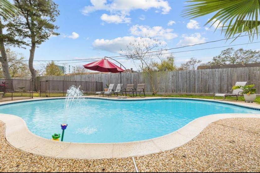 This photo showcases a backyard with a sparkling pool, surrounded by a fence for privacy. The area features lounge chairs and a red umbrella, creating a relaxing outdoor space ideal for entertaining or unwinding.