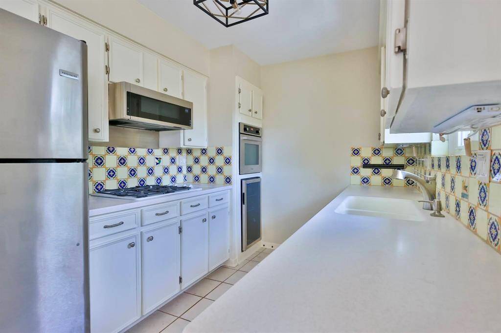 Bright, compact kitchen with white cabinets and colorful patterned backsplash. Features stainless steel appliances, including a refrigerator and built-in oven. The counter space is ample, and there's a modern range hood above the stove.