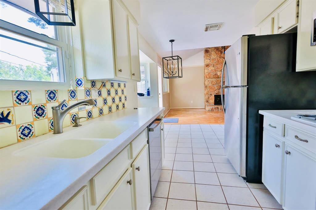 This photo showcases a bright kitchen with white cabinetry and colorful tile backsplash. The kitchen opens to a dining area with a stone accent wall and wood flooring, creating a cozy and inviting space.