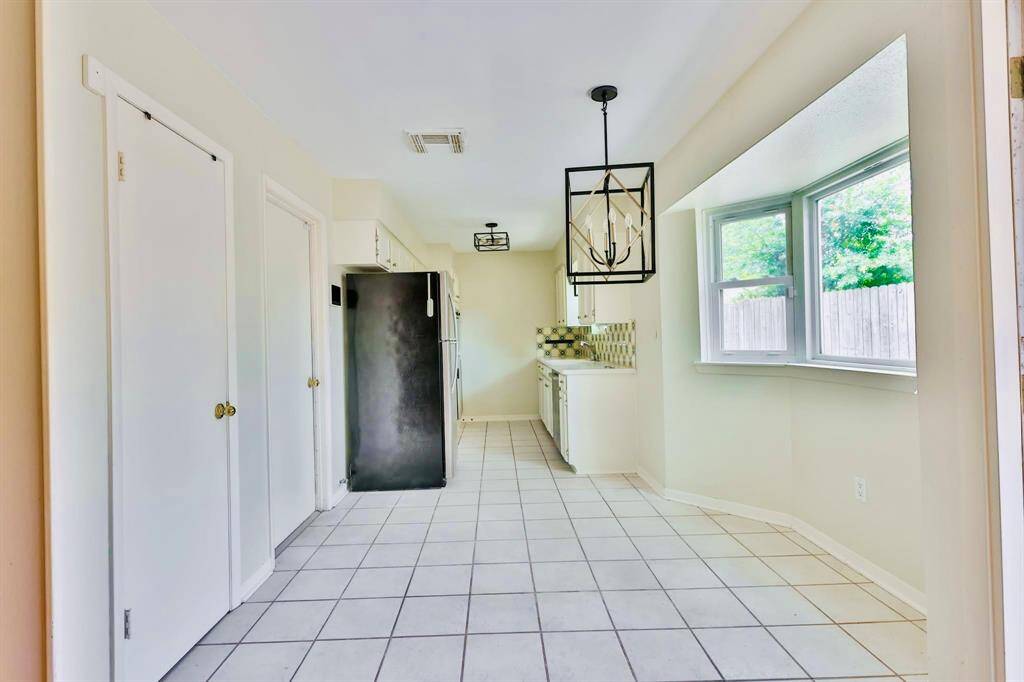 Bright, spacious kitchen with white cabinetry and tile flooring. Features a modern light fixture, stainless steel appliances, and a large bay window offering plenty of natural light.