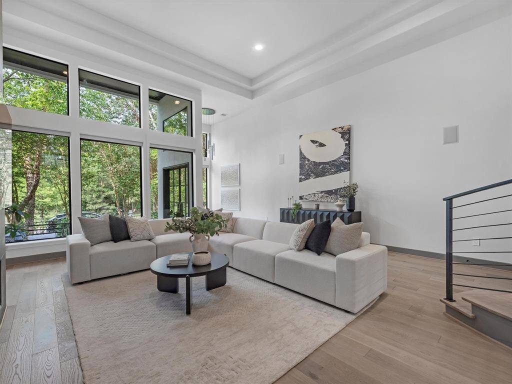 The spacious living room features large windows offering a beautiful view of the trees, a modern open layout, and stylish neutral decor with a contemporary feel. Perfect for natural light and relaxation.