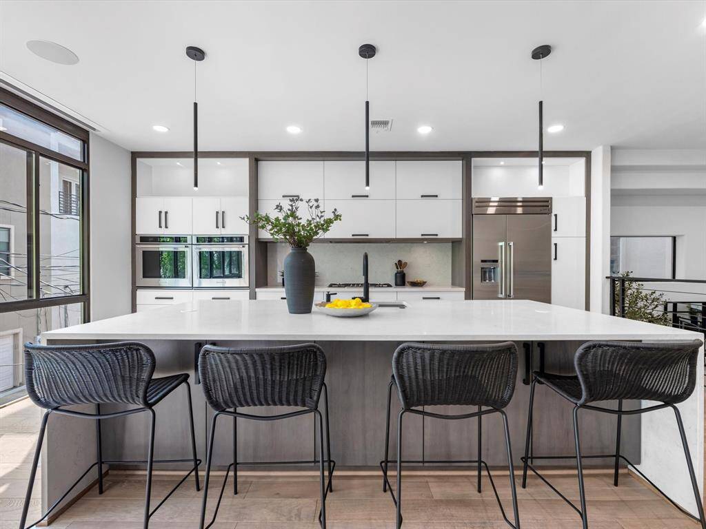 This modern kitchen features a large island with seating, sleek cabinetry, stainless steel appliances, and pendant lighting, offering a bright and stylish space for cooking and entertaining.