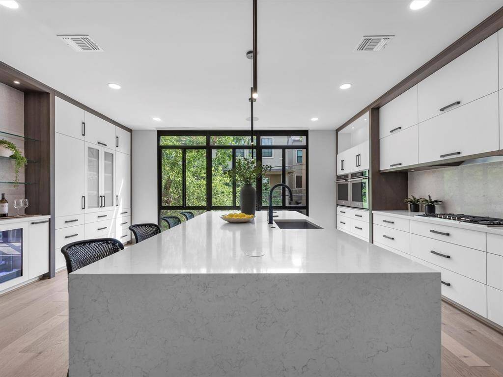 This modern kitchen features a spacious island with a sleek countertop, ample cabinetry, and large windows providing natural light. The open layout includes built-in appliances and contemporary finishes, offering a stylish and functional space.