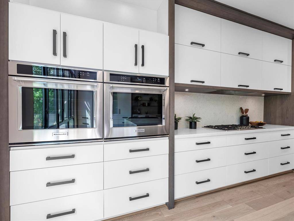 The modern kitchen features sleek white cabinetry with black handles, stainless steel double ovens, and a built-in Gas cooktop, creating a clean and contemporary look.