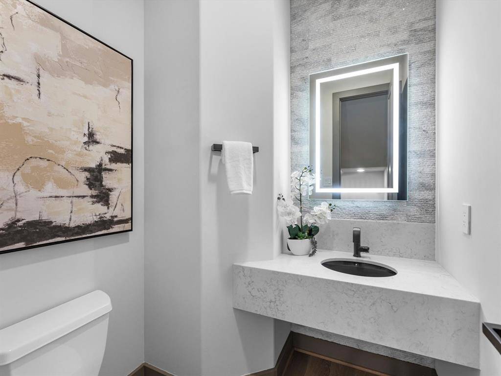 The powder room features a modern design with a sleek, illuminated mirror, elegant stone countertop, and contemporary fixtures. Soft lighting adds a touch of sophistication.