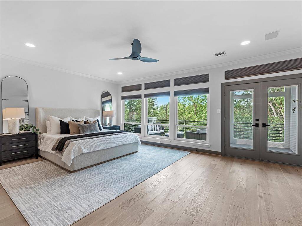 The spacious primary bedroom features large windows and glass doors offering abundant natural light and views of greenery. It includes a stylish ceiling fan, elegant wood flooring, and access to a private balcony. The room is tastefully decorated with a neutral color palette, enhancing its modern and serene ambiance.