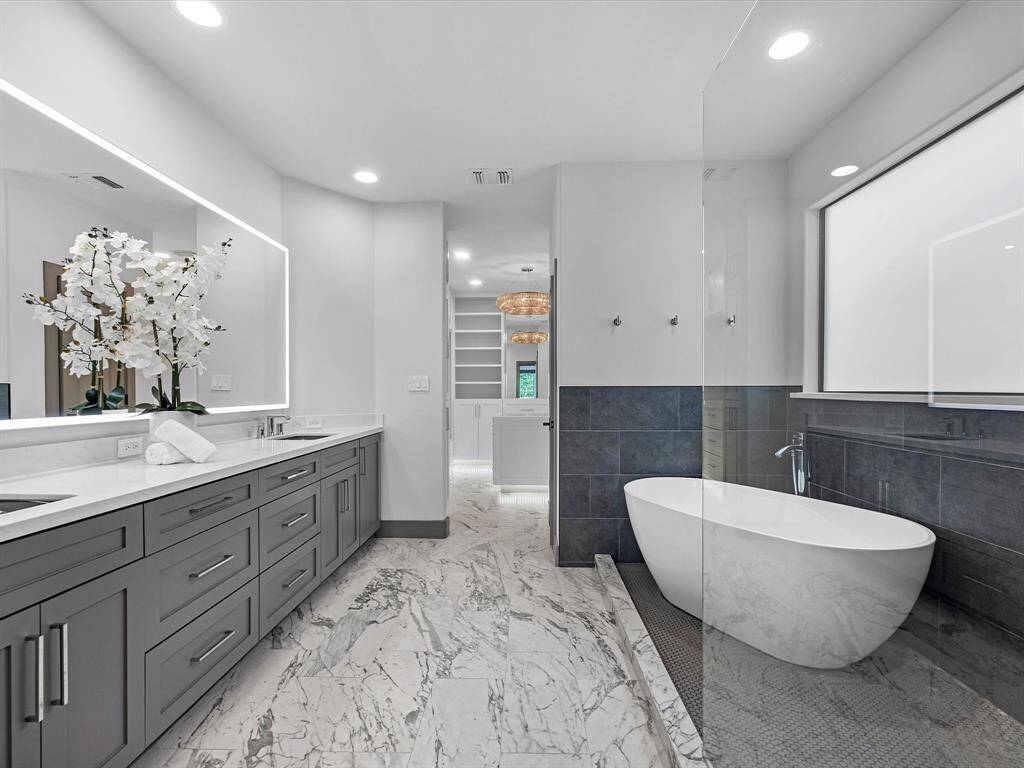The bathroom features a modern design with marble flooring and a large vanity with ample storage. It includes a sleek freestanding bathtub and a spacious walk-in shower, creating a luxurious and relaxing atmosphere.