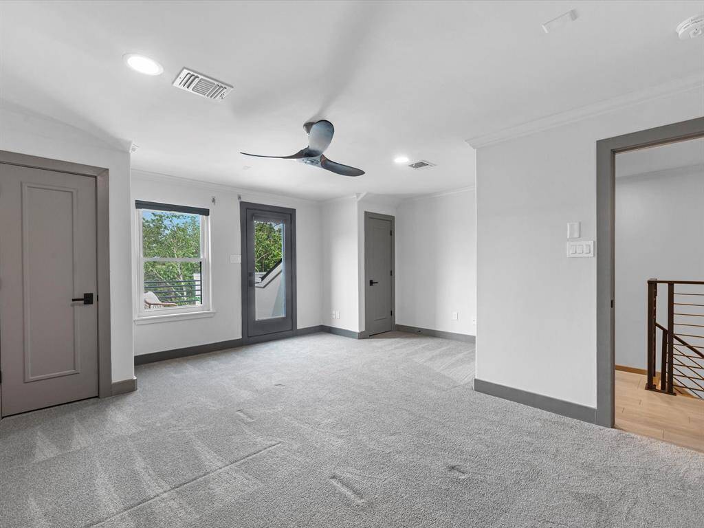 Bedroom 2 is spacious and light-filled and features neutral carpeting, modern gray doors, and a ceiling fan. Large windows offer natural light, while an open doorway with a railing gives access to a private balcony.