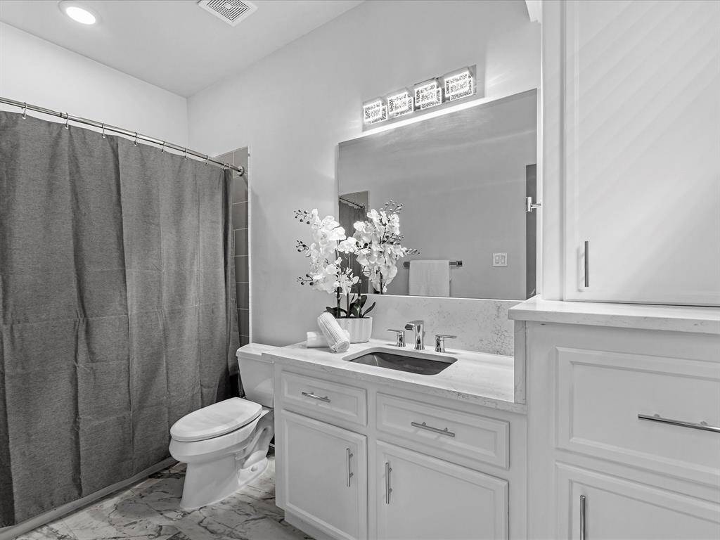 The bathroom features a modern design with a large mirror, ample counter space, and elegant cabinetry. It includes a bathtub with a shower curtain and stylish lighting above the sink.