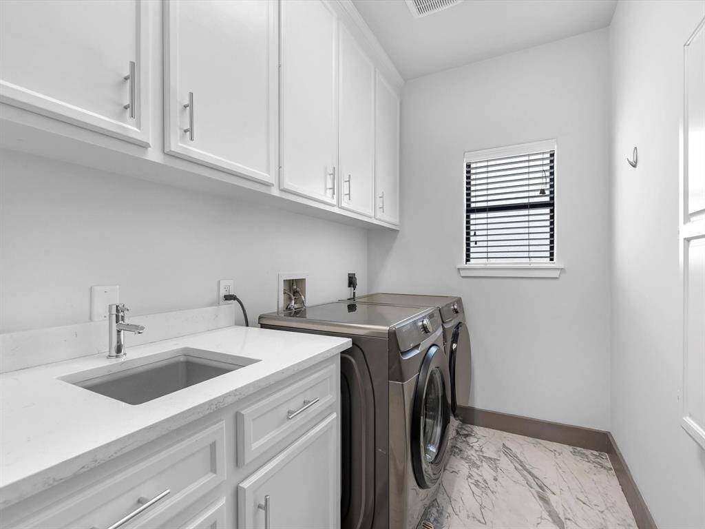 The laundry room features modern appliances, ample cabinet storage, and a sleek countertop with a built-in sink. It has a clean, bright design with a window for natural light.