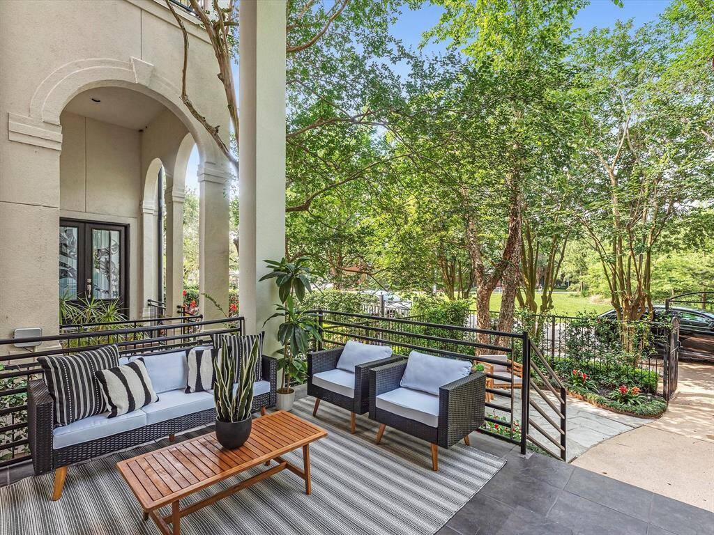 This inviting patio features space for modern outdoor furniture, lush greenery, and a spacious tiled floor, perfect for relaxing or entertaining. The area is bordered by elegant columns and overlooks a serene, tree-filled landscape.