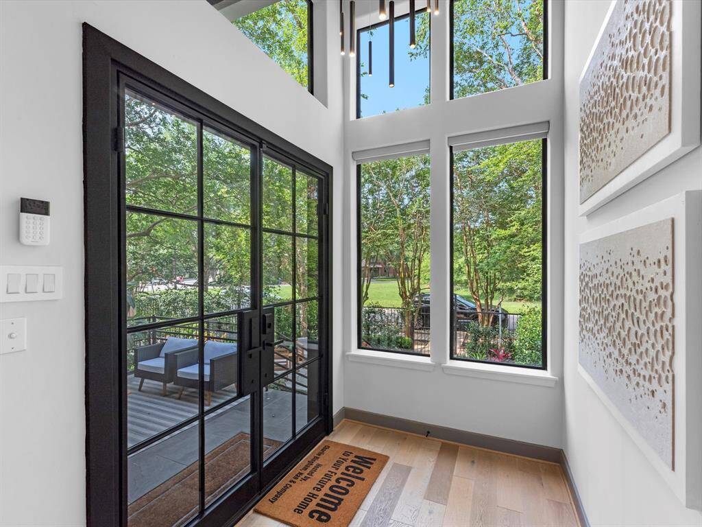 Bright entryway with large windows offering abundant natural light and views of greenery. Features sleek black-framed glass doors, light wood flooring, make for a welcoming atmosphere.