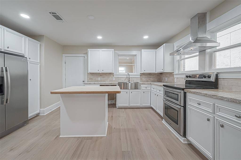 Stainless steel appliances include refrigerator, dishwasher, electric range with double ovens and hood.