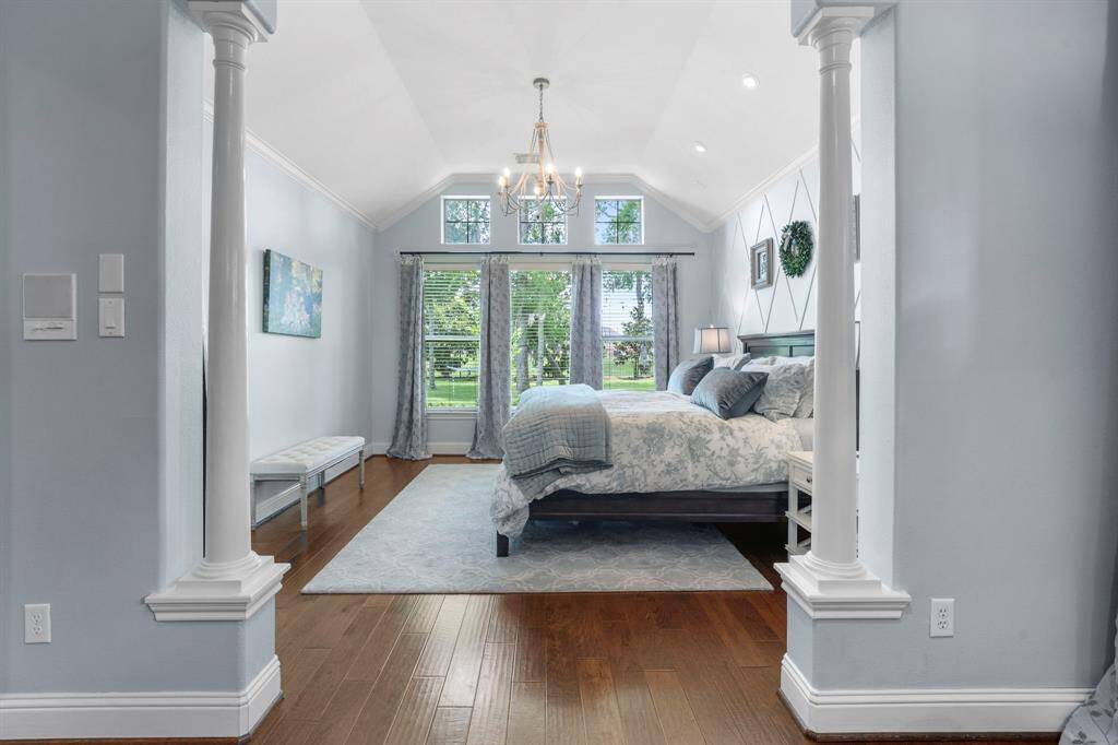 Step into the sanctuary of theprimary bedroom featuring beautiful floors, high ceilings, crown molding, pillars, and a chandelier.