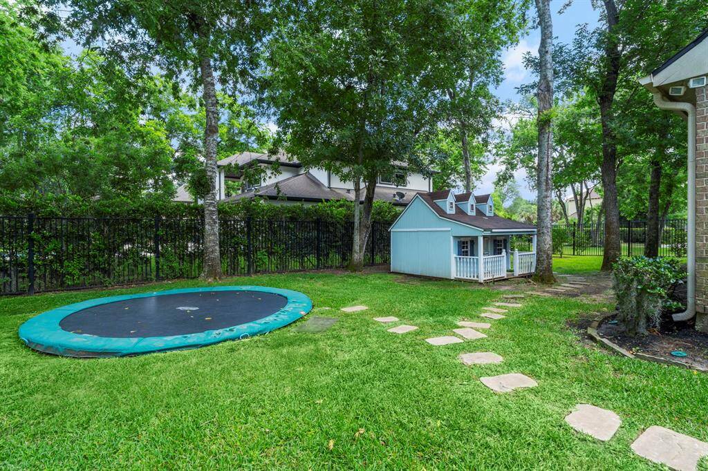 The backyard has a paved walkway and tall trees to provide plenty of shade over the trampoline and playhouse.