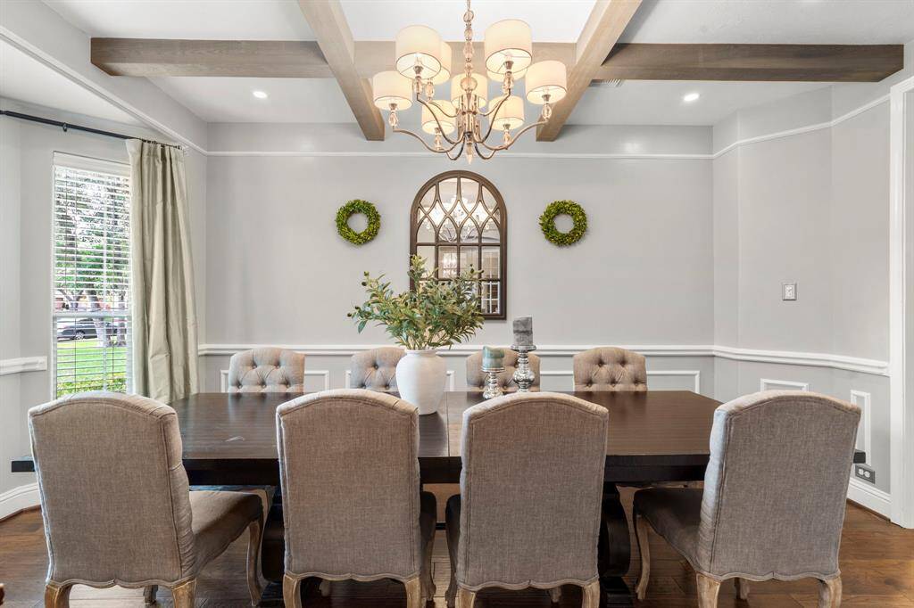 This dining room is bathed in naturallight streaming through expansivewindows and features beams on the ceiling, recessed lighting, chandelier, and chair rail.