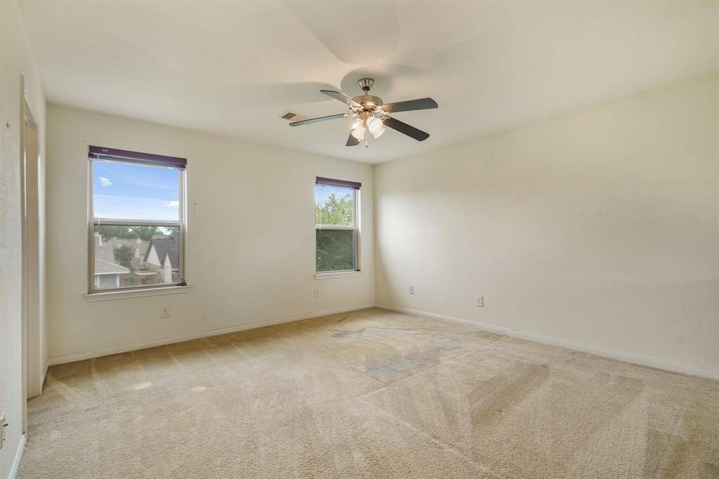 Spacious primary bedroom with large windows, carpet floors, and a ceiling fan.