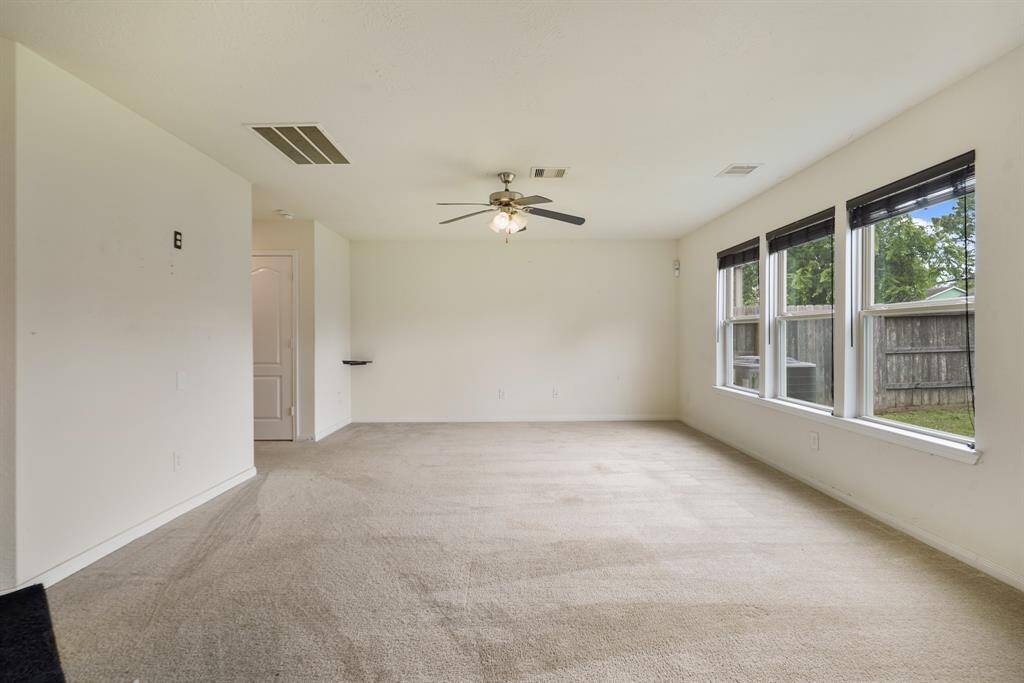 This grand living area has large windows, carpet floors, and a ceiling fan.