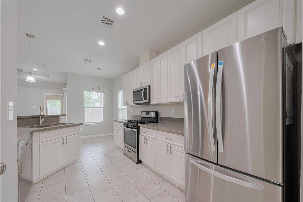 The kitchen features stainless steel appliances, a refrigerator included, white cabinetry, and light tile flooring. It has a modern open layout with ample natural light and pendant lighting above the bar counter.