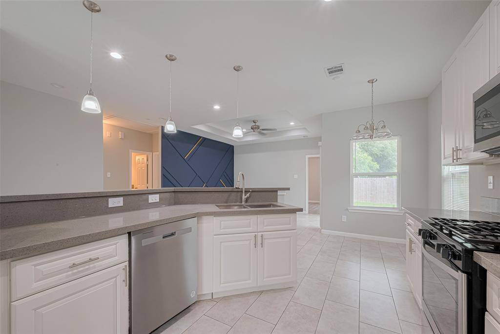 The modern kitchen features white cabinetry, stainless steel appliances, and a spacious island with pendant lighting. The open design flows into a bright living area with large windows and contemporary accents, creating a welcoming atmosphere.