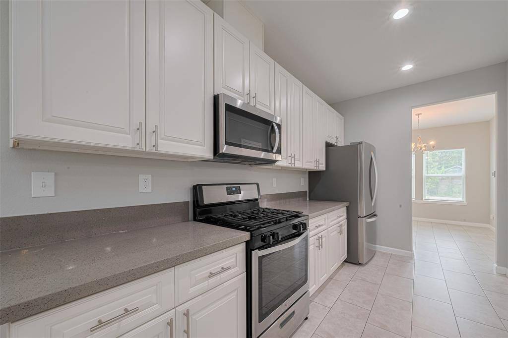 Modern kitchen with stainless steel appliances, white cabinetry, and quartz countertops. Bright and spacious with tile flooring and recessed lighting, leading to a dining area with natural light.