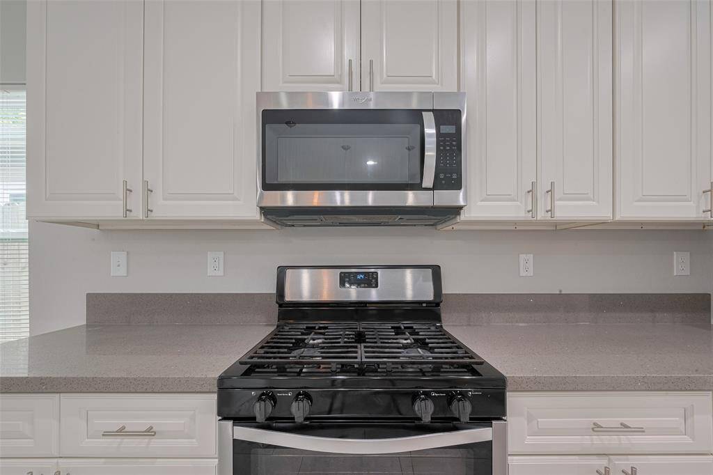This kitchen features modern stainless steel appliances, including a gas stove and microwave. It has quartz countertops and ample white cabinetry for storage.