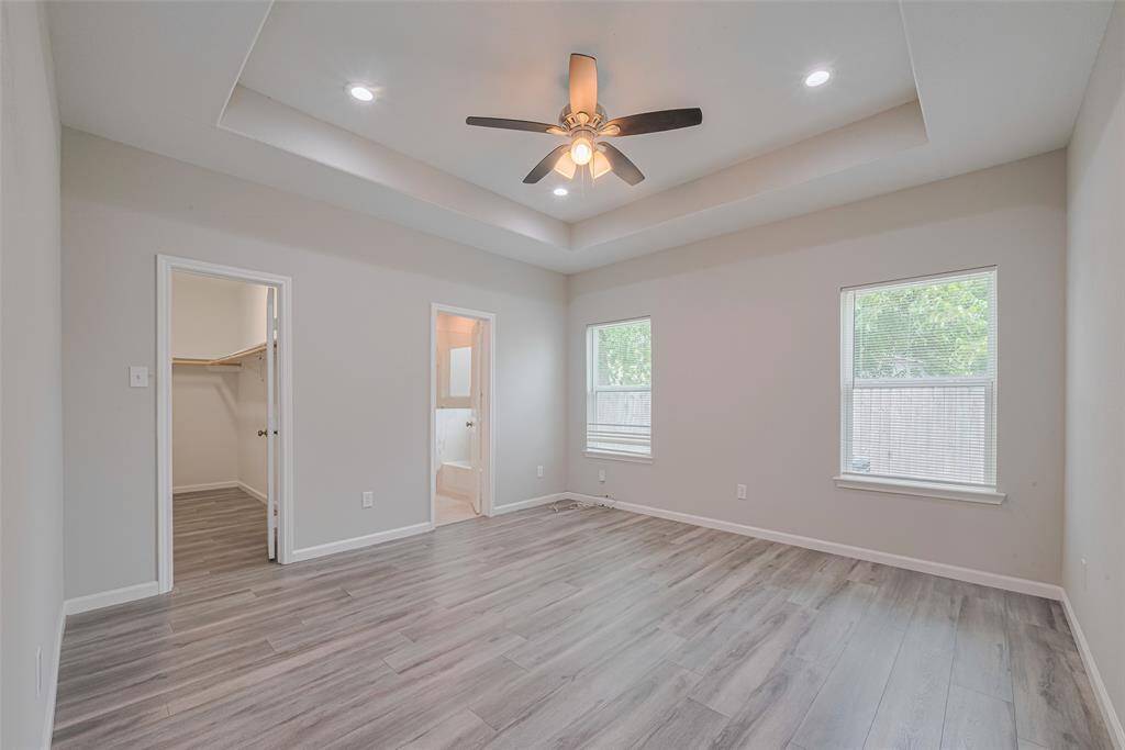 This room features modern gray flooring, neutral walls, and a recessed ceiling with recessed lighting and a ceiling fan. It includes two large windows providing natural light, a walk-in closet, and an en-suite bathroom for convenience.