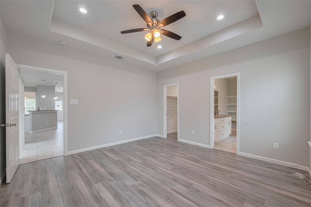 The showcases a spacious, well-lit room with modern wood flooring, a ceiling fan, and recessed lighting. It features two doorways leading to additional rooms.