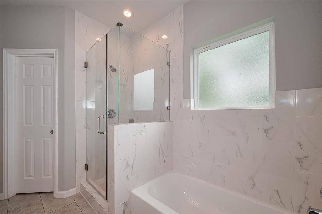 This bathroom features a modern design with a glass-enclosed shower and a separate bathtub. The walls and bathtub surround are finished with elegant marble-patterned tiles, and there's a frosted window for natural light and privacy.