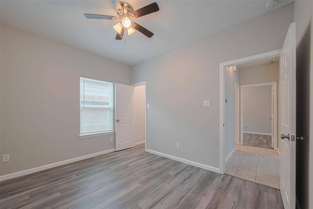 The third bedroom features laminate flooring, neutral walls, a ceiling fan, and ample natural light from a window. It has access to an adjoining room through a door, with a blend of tile and laminate flooring throughout.