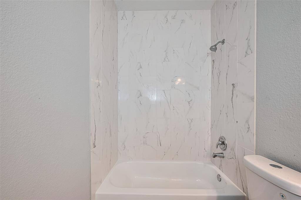 Modern bathroom with a white bathtub and a sleek showerhead. The walls are adorned with elegant marble-patterned tiles, creating a clean and sophisticated look.