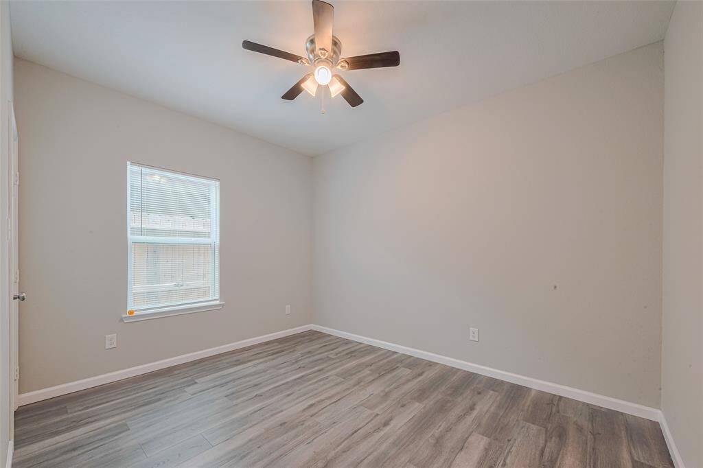 The third bedroom features a neutral color palette with light gray walls and wood-look flooring. It includes a ceiling fan and a window that provides natural light, creating a bright and airy atmosphere suitable for a bedroom or office.