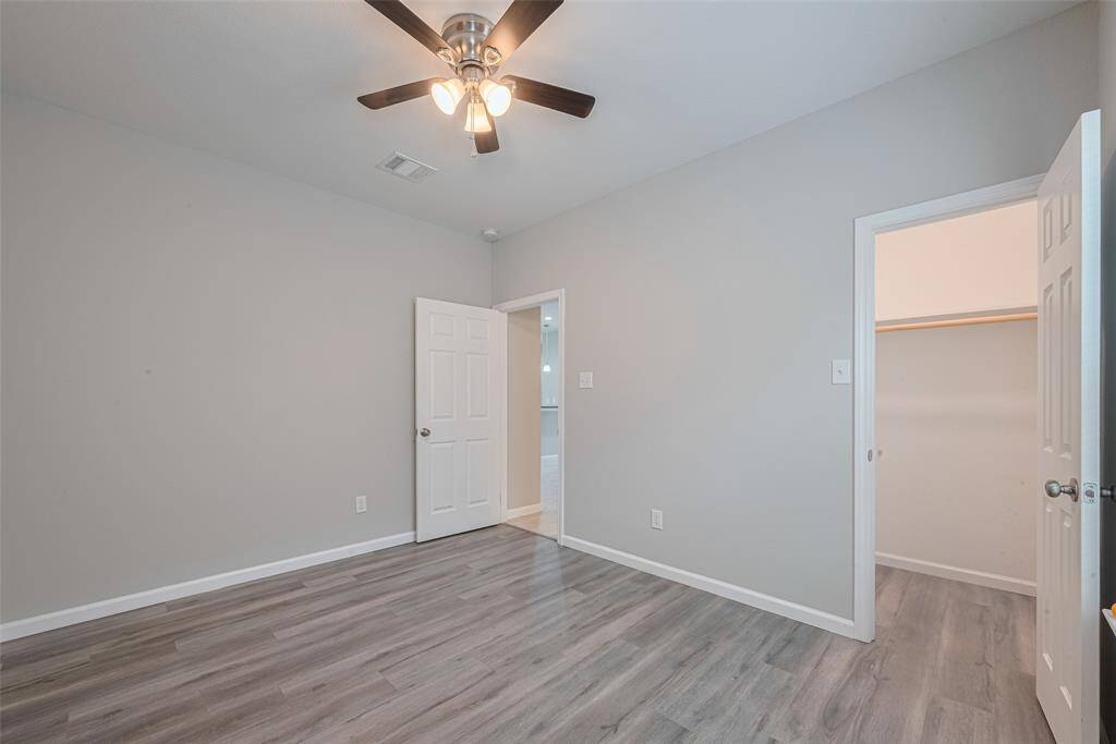 The second bedroom features light gray walls, wood-look flooring, and a ceiling fan with lights. It has a closet and an open door leading to an adjacent space, creating a clean and modern look.