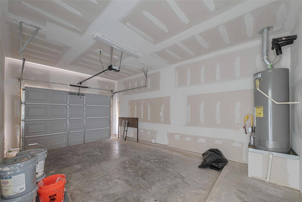 The spacious garage has with wheel stop, finished walls, and a concrete floor. It features a garage door with an automatic opener, a water heater in the corner, and some storage items. Ideal for parking or extra storage space.