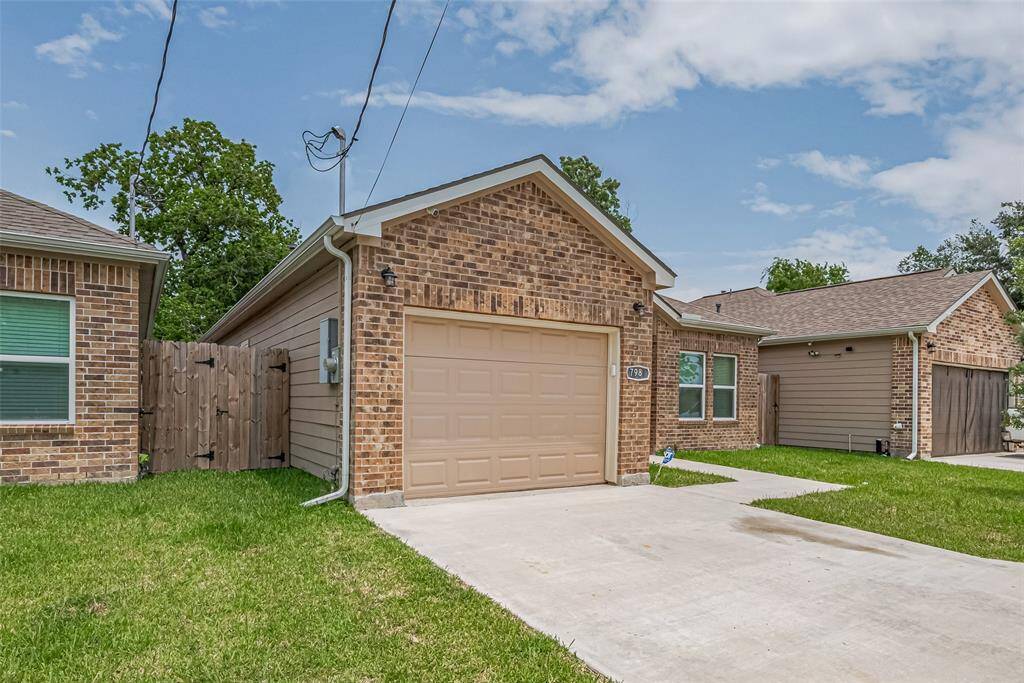 The charming brick house features a well-maintained driveway and fenced yard. It's situated in a quiet neighborhood and offers a cozy, inviting facade with a neatly manicured lawn.