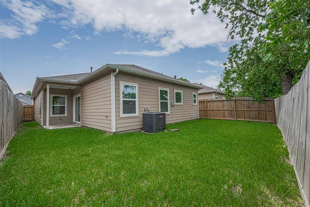 Well-maintained, fully fenced backyard with lush green grass, a small patio area, and a modern single-story house exterior. Perfect for outdoor activities and privacy.