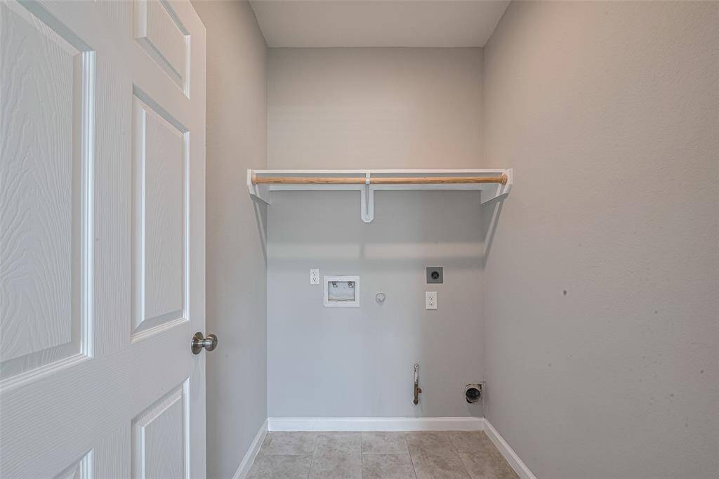 This photo shows a laundry room with hookups for a washer and dryer. It features a shelf for storage and neutral-colored walls, providing a clean and functional space.