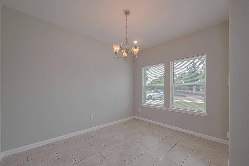 Bright dining room with neutral walls, tiled flooring, and a stylish chandelier. Large windows provide ample natural light and views of the front yard.