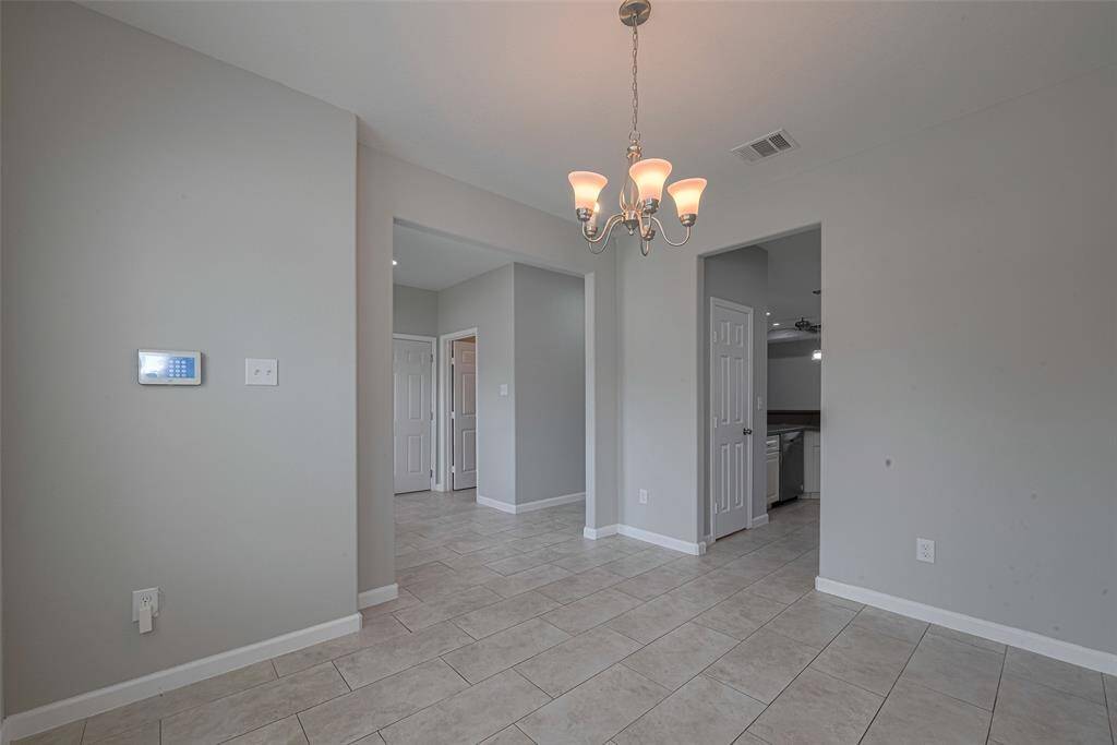 Modern interior space with light gray walls and tiled flooring. A simple chandelier hangs from the ceiling, adding elegance. The area has multiple doorways leading to other parts of the home, creating an open and inviting flow.
