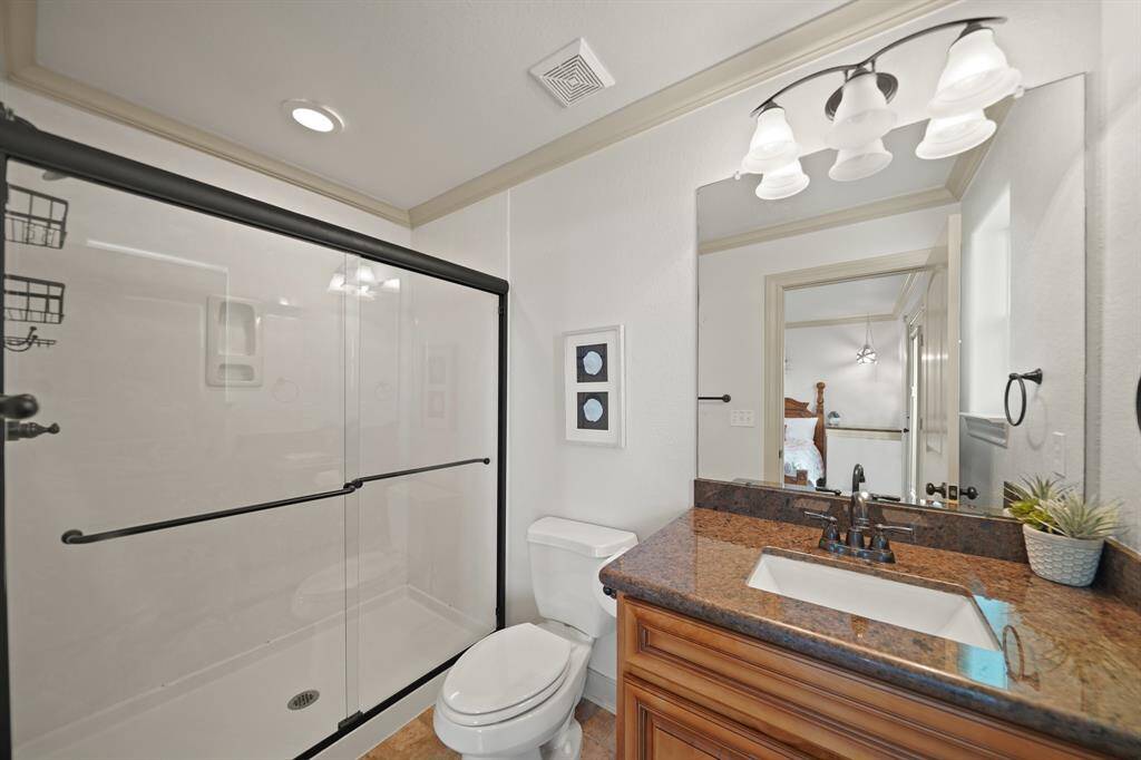 Attached to a guest suite, this bathroom features a granite vanity, walk-in shower with sliding glass doors, and modern lighting.