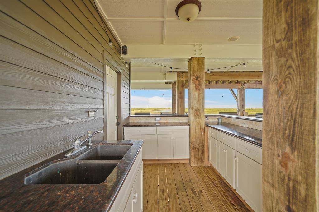 The lower level boasts a large, covered outdoor space complete with string lights, a spacious bar with granite counters, ample seating, and a fully functional outdoor kitchen.