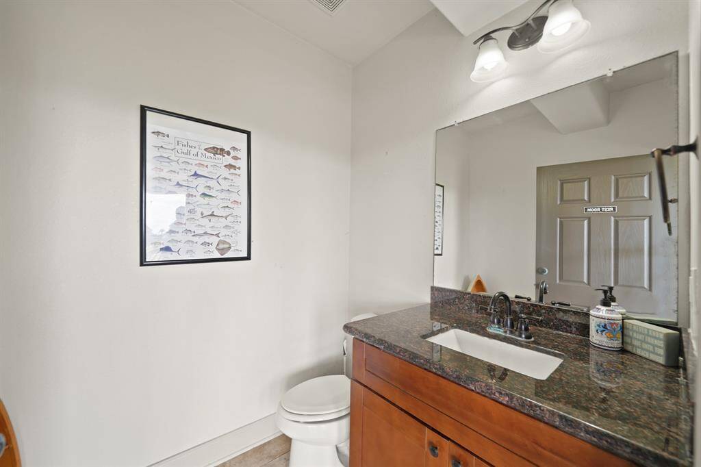 Conveniently located on the lower level, this charming half bath features a granite vanity, rich wood cabinetry, updated fixtures, and coastal accents—perfect for guests or quick clean-ups after the beach.