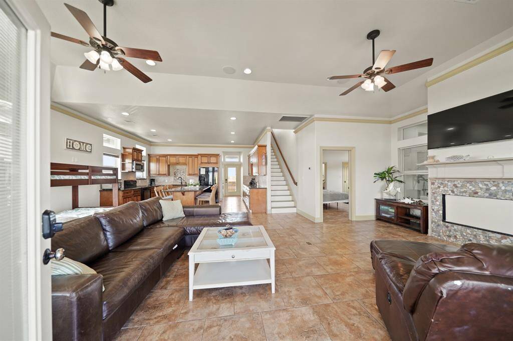 Spacious open-concept living area features soaring ceilings, dual ceiling fans, and a cozy fireplace surrounded by beautiful mosaic tilework.