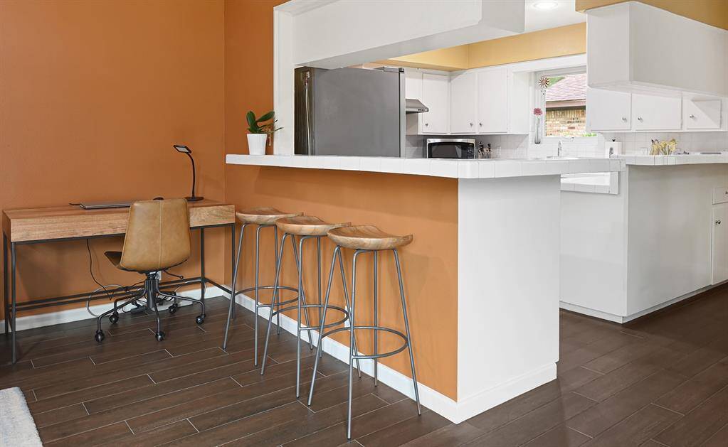 Ample room for a cozy desk space, and a breakfast bar with stylish stools. The space is open and bright, complemented by white cabinetry.