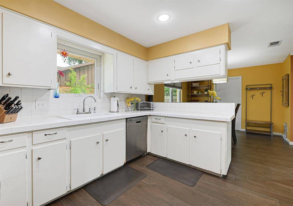 The kitchen features bright white cabinets, a window over the sink with a view, and wood-look tile flooring. A functional layout includes ample counter space and modern SS appliances.