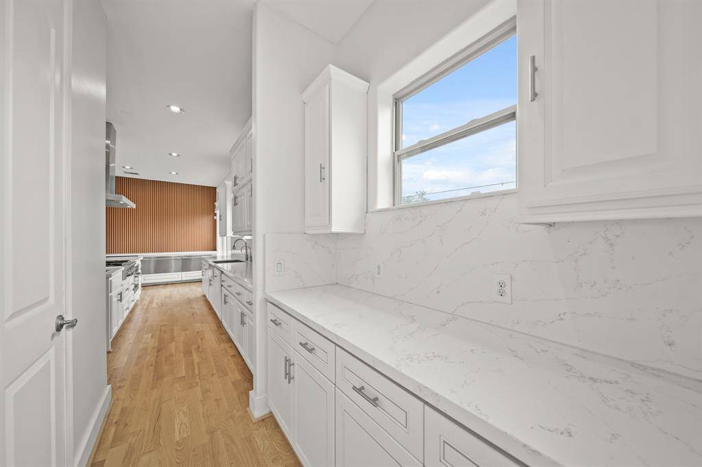 The Butler's Pantry offers a Quartz Topped Counter, White Painted Raised Panel Cabinets and Drawers, LED Recessed Lighting, Walk in Pantry with Multiple Shelves, Fresh Designer Paint, and Brand New (April 2025) Refinished Natural Hardwood Floors.